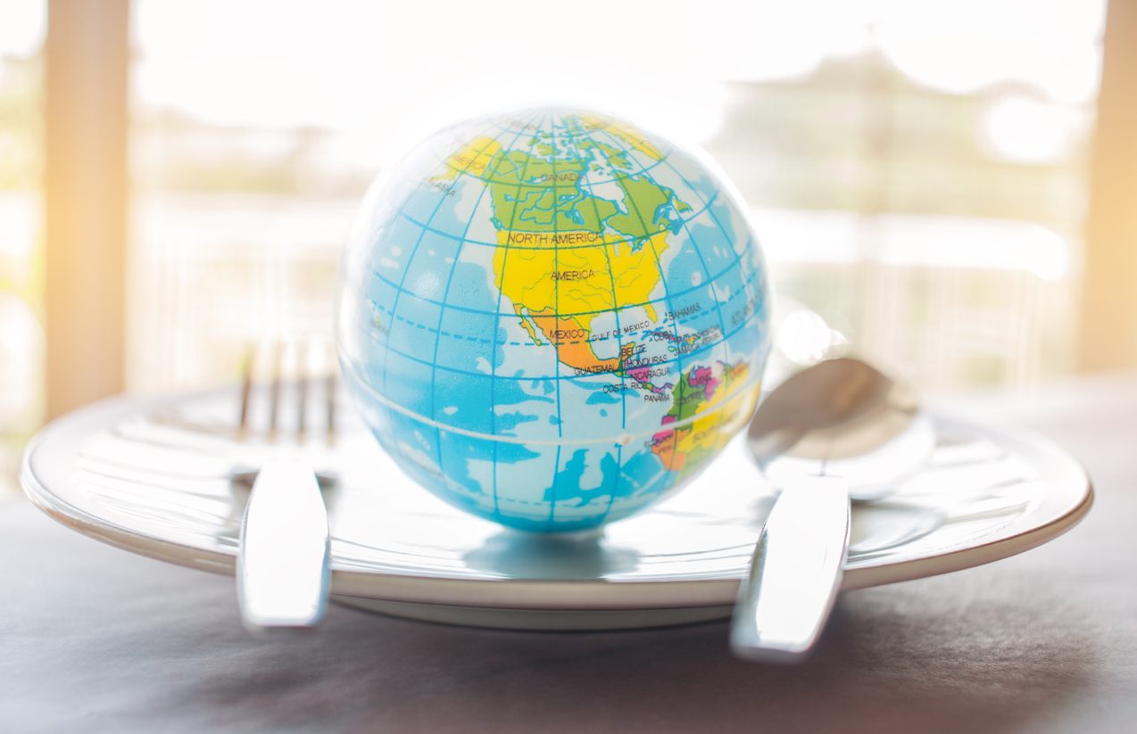 Globe model on a plate with a fork and spoon on each side, symbolizing international cuisine.